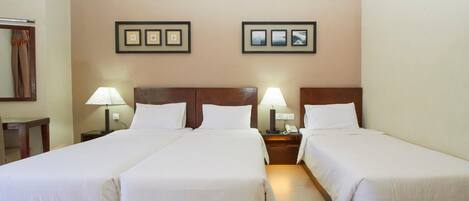 A hotel room with two single beds, a wooden headboard, bedside lamps, and framed pictures on the wall.