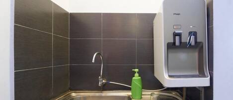 Un baño con lavamanos, grifo, dispensador de jabón y unidad dispensadora de agua etiquetada 'Magic'.