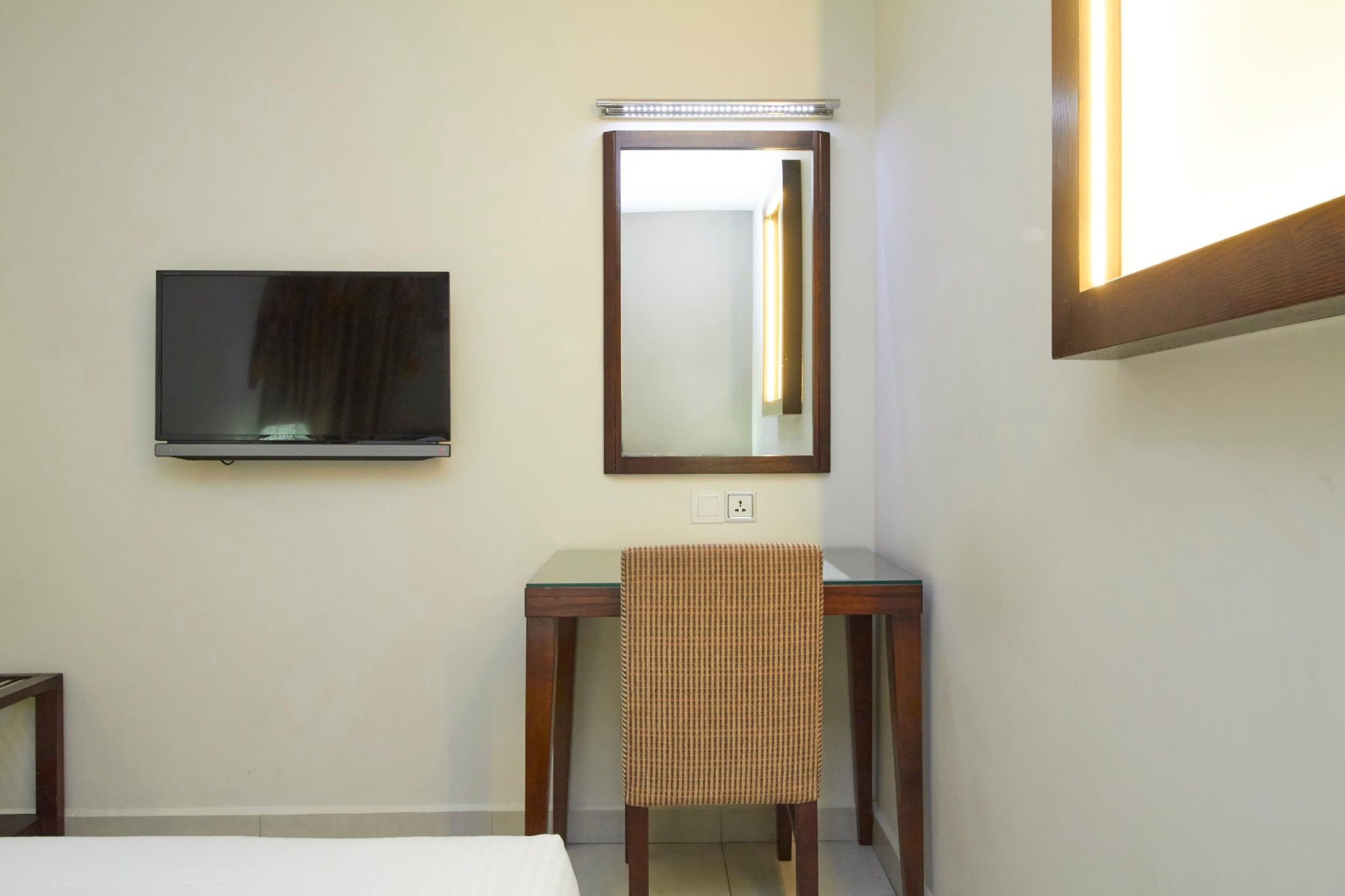 A hotel room with a bed, a TV mounted on the wall, a desk with a chair, and a mirror.