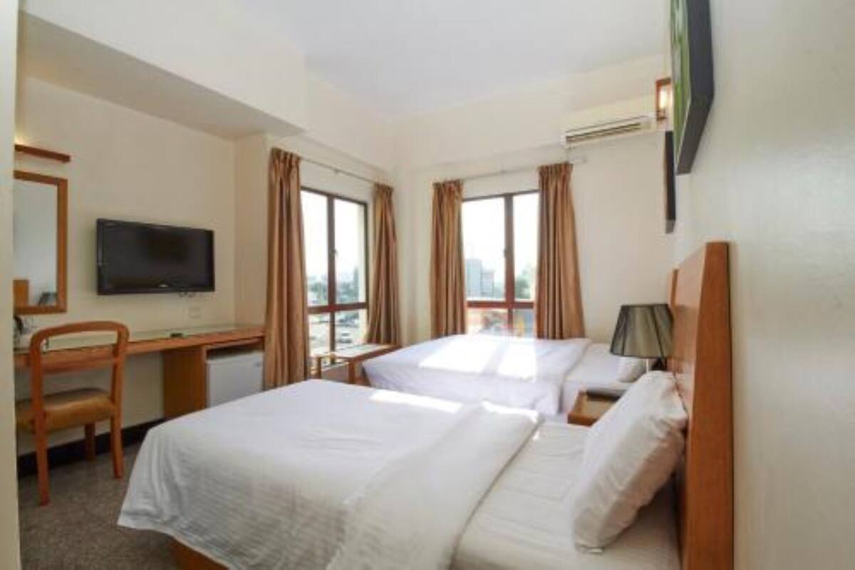 A hotel room with two beds, a desk, a chair, a television, and large windows with curtains.