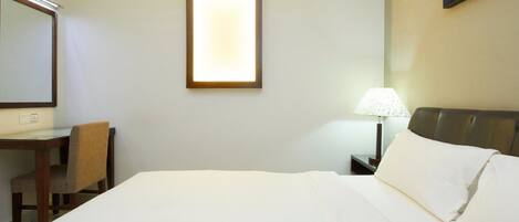 A hotel room with a bed, a desk, a chair, a lamp, and a wall-mounted light fixture.