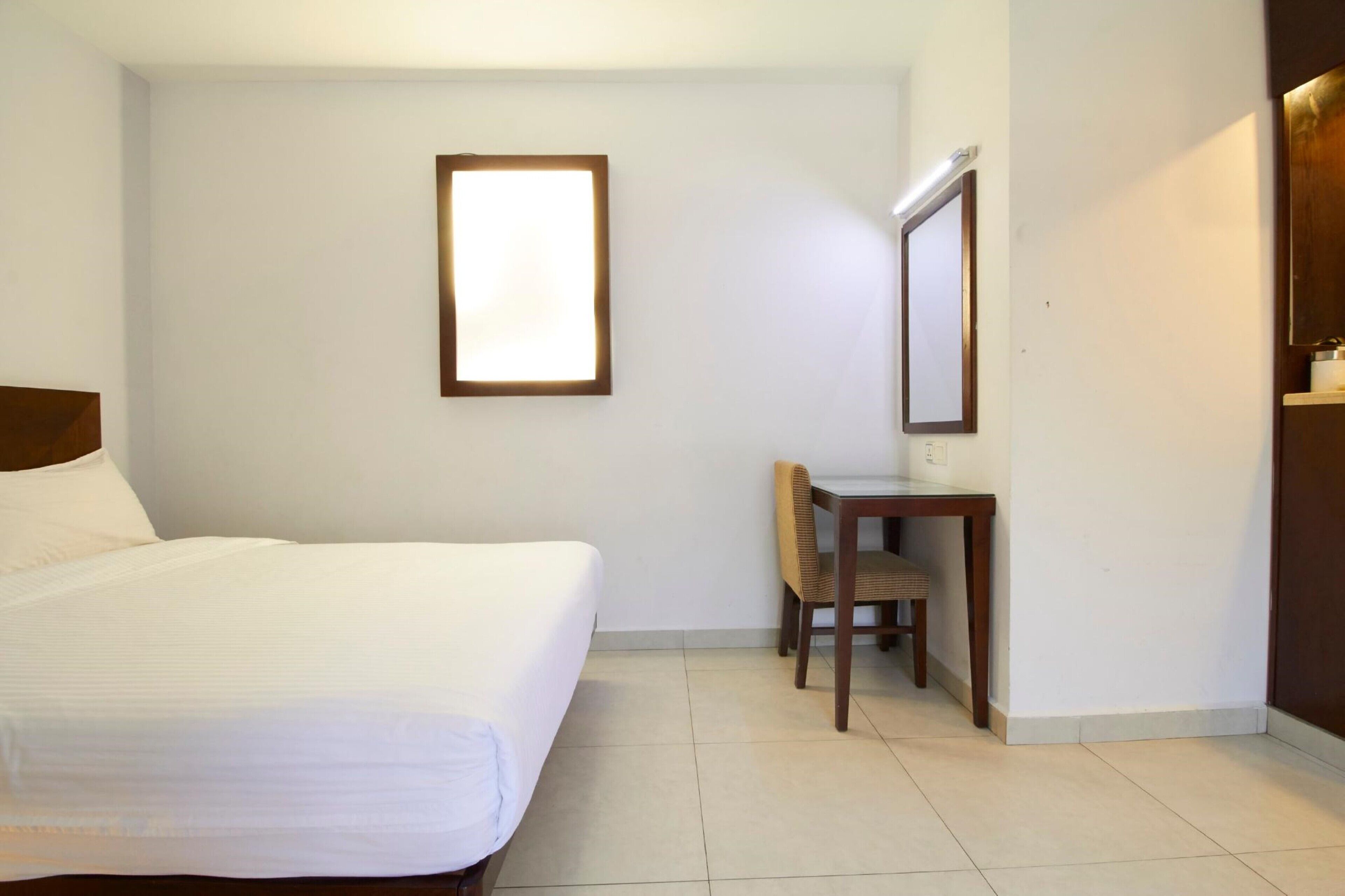 Une chambre d’hôtel comprenant un lit, un bureau avec une chaise, un miroir et une armoire.