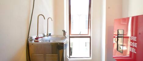 A bathroom with a sink, a red fire hose reel, and a window.