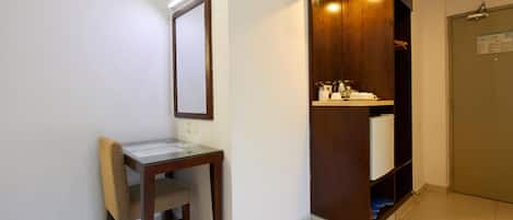 Habitación de hotel con escritorio de madera, espejo, mueble empotrado de madera con lavamanos y una puerta con un aviso.