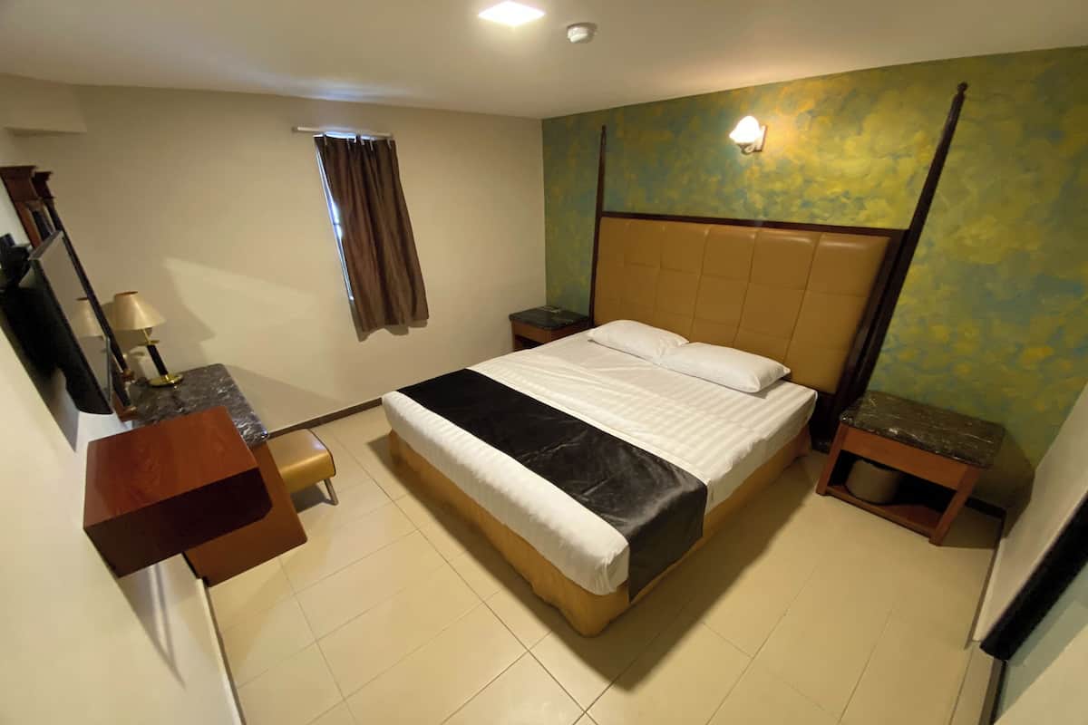 Une chambre d’hôtel avec un lit, des tables de chevet, un bureau, un miroir et une fenêtre avec des rideaux.
