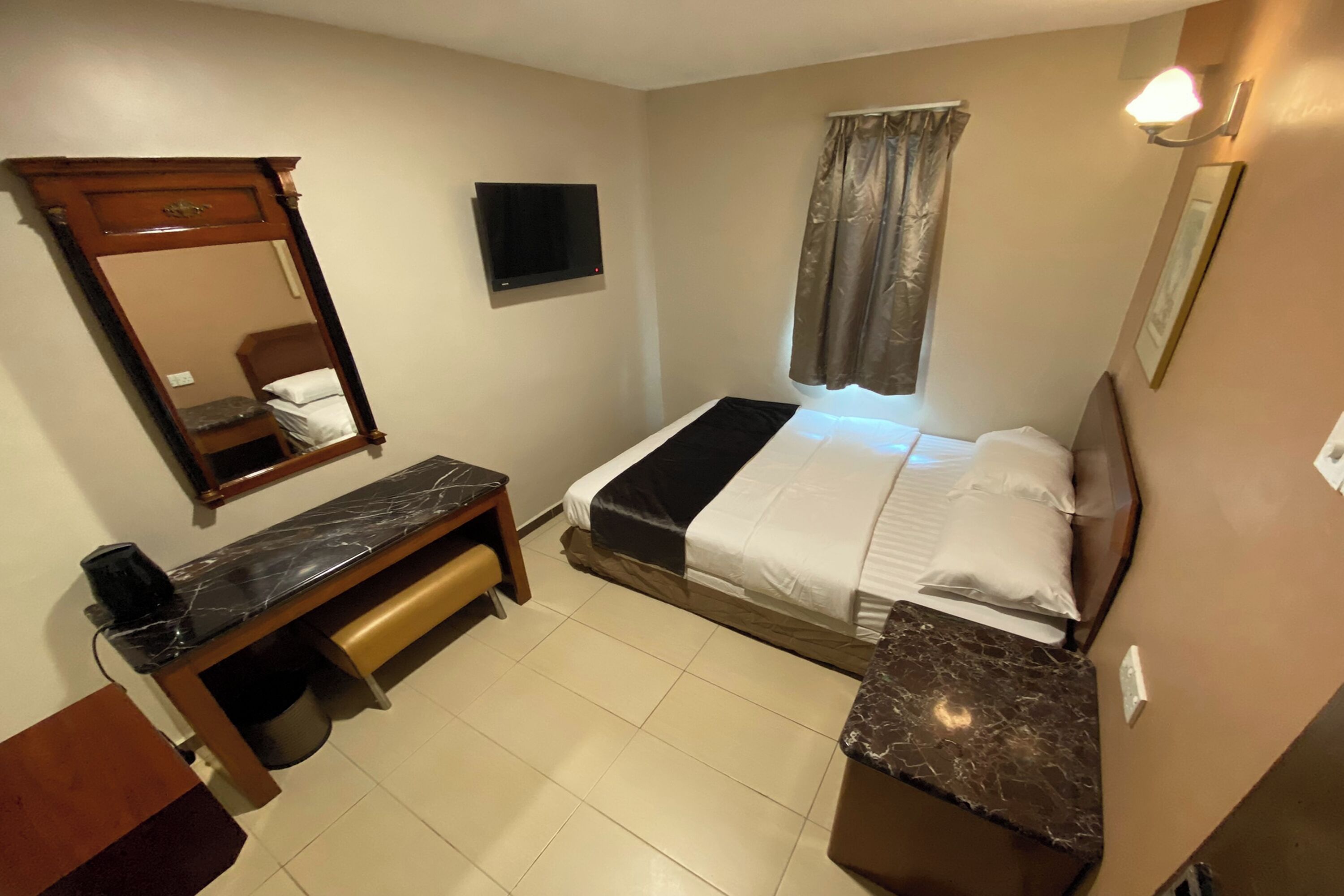 A hotel room with a bed, a desk, a mirror, a TV, and a window with curtains.