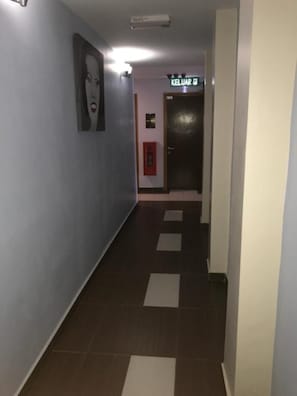 Un corridoio con un pavimento a scacchi, una segnaletica con scritto 'KELUAR' e un segnale di uscita di emergenza rosso.