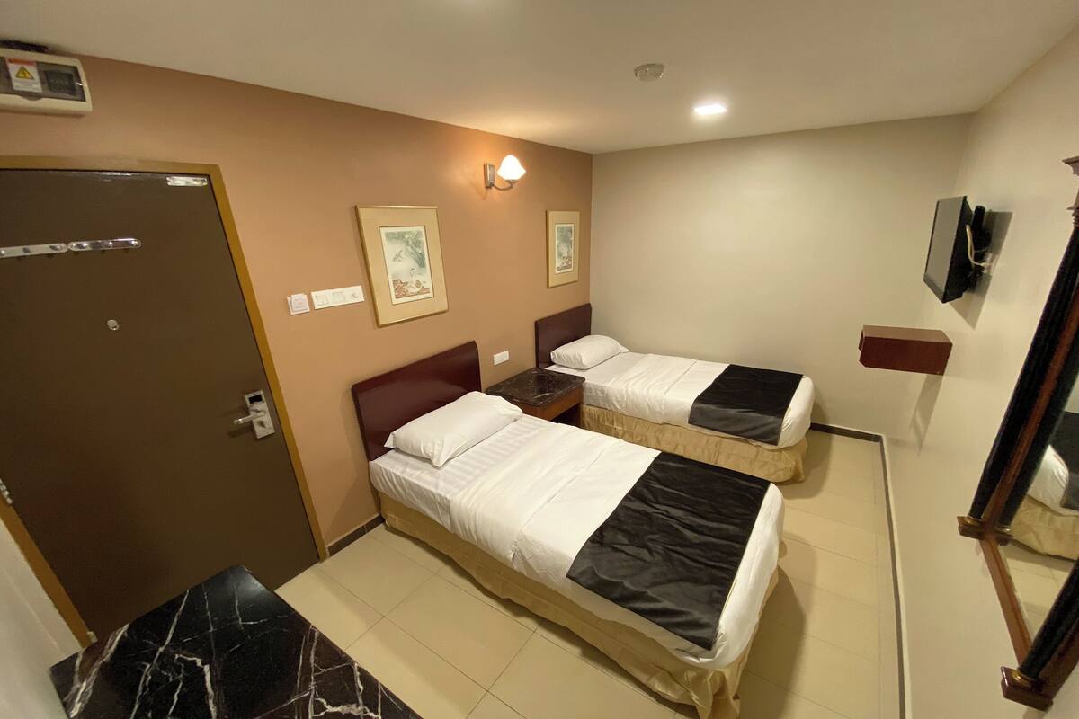 Une chambre d’hôtel avec deux lits, une porte, une petite table et un téléviseur fixé au mur.