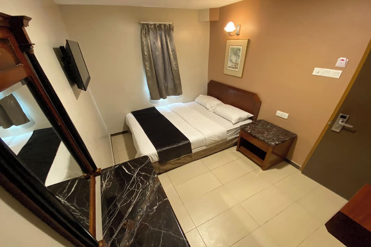 Une chambre d’hôtel comprenant un lit, une petite table de chevet, un miroir, une fenêtre avec des rideaux et un luminaire fixé au mur.