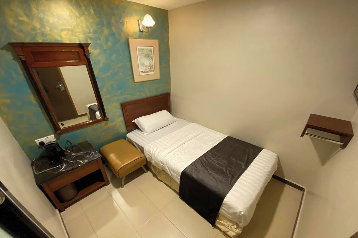 Une chambre d’hôtel comprenant un lit, une table de chevet, un banc, un miroir et une étagère fixée au mur.