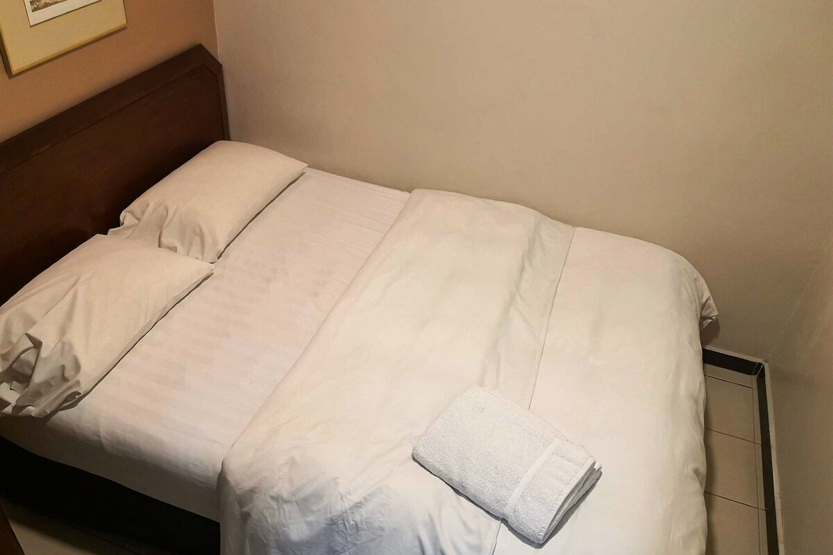 A single bed with white bedding, a wooden headboard, and a folded towel on the footboard.