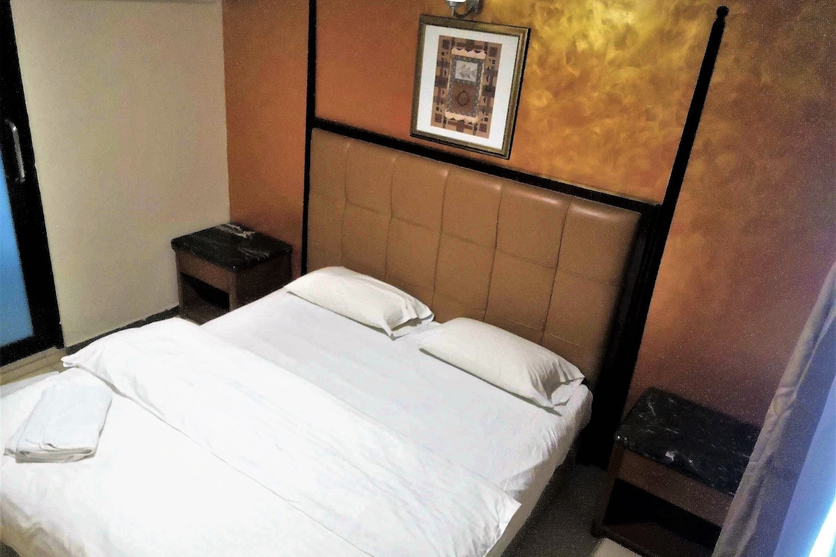 Une chambre d’hôtel avec un lit, une table de chevet, un tableau encadré au mur et un luminaire fixé au mur.