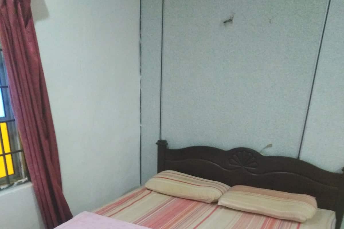 Una cama individual con una manta rosa y ropa de cama a rayas en una habitación con paredes lisas y una ventana con cortinas rojas.