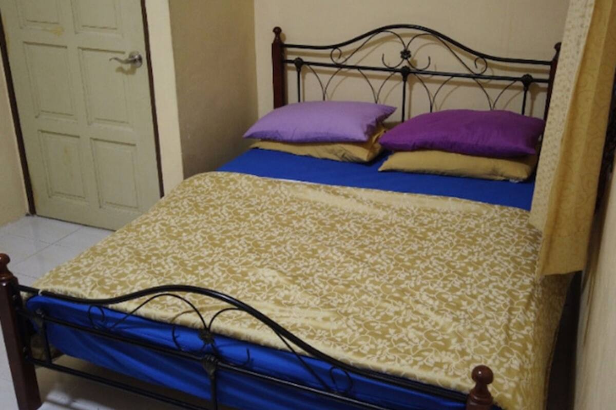 A single bed with a patterned bedspread, two pillows, and a metal headboard.