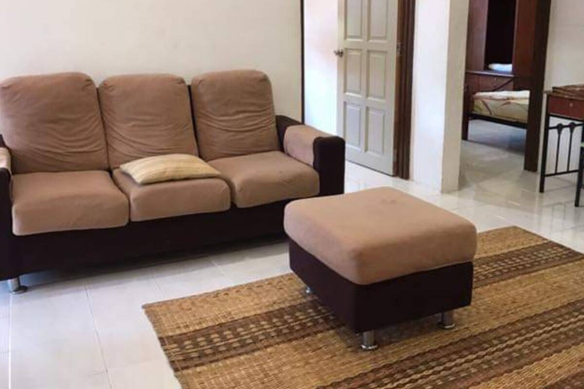 A living room with a beige sofa, a matching ottoman, and a patterned rug.