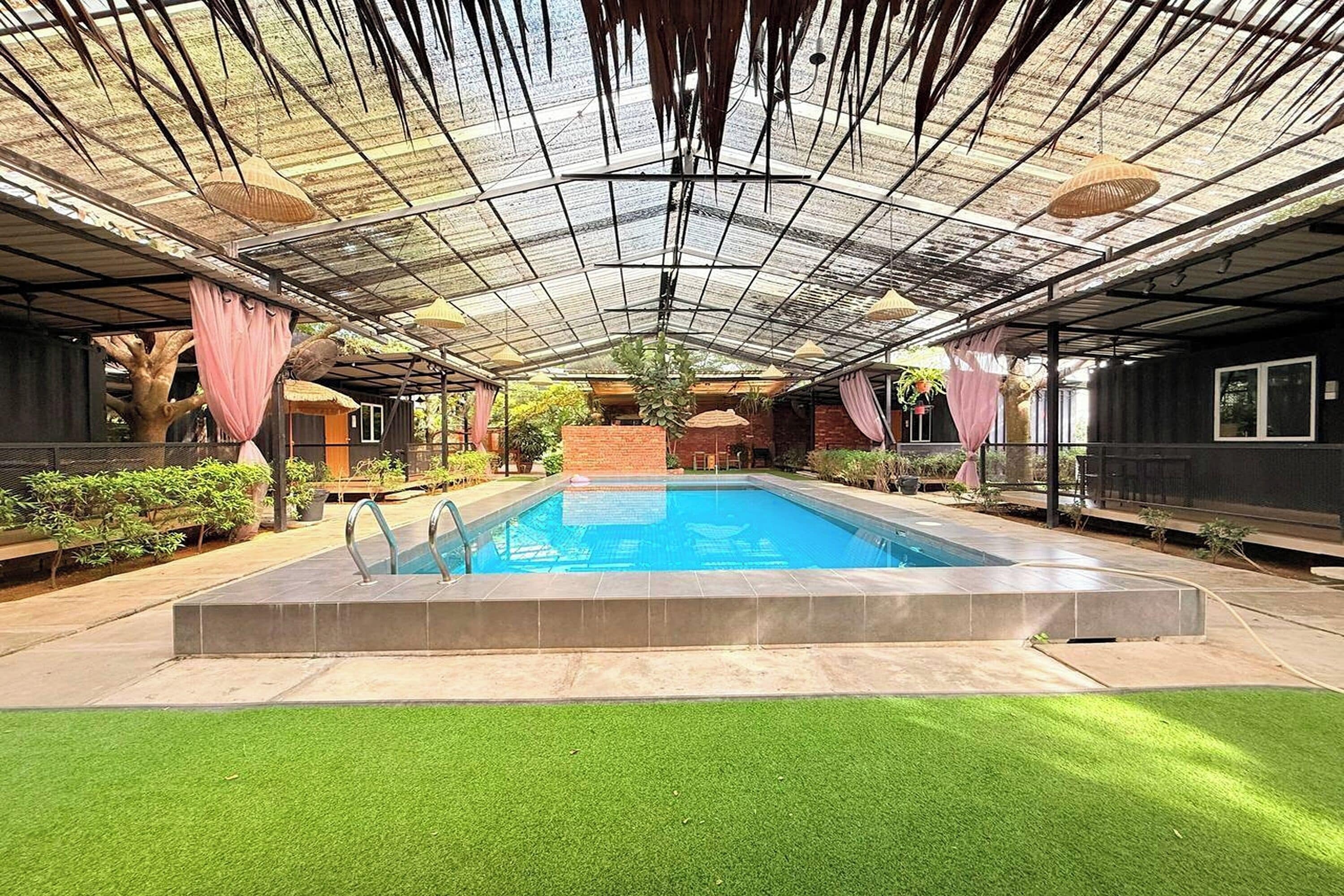 A swimming pool with a glass ceiling, surrounded by greenery and a brick structure.