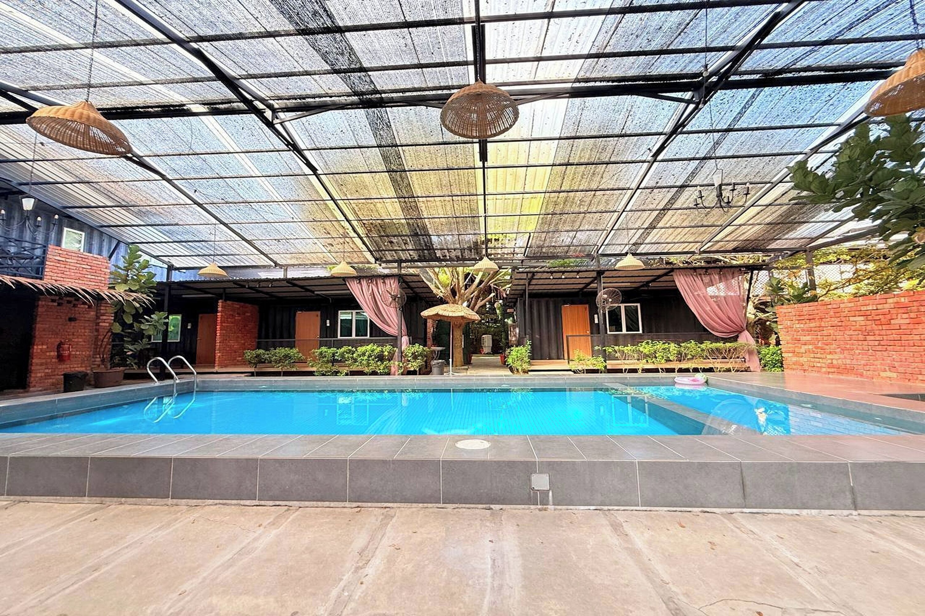 An indoor swimming pool with a glass ceiling, surrounded by brick walls and potted plants.