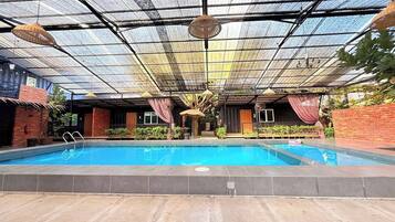 An indoor swimming pool with a glass ceiling, surrounded by brick walls and potted plants.