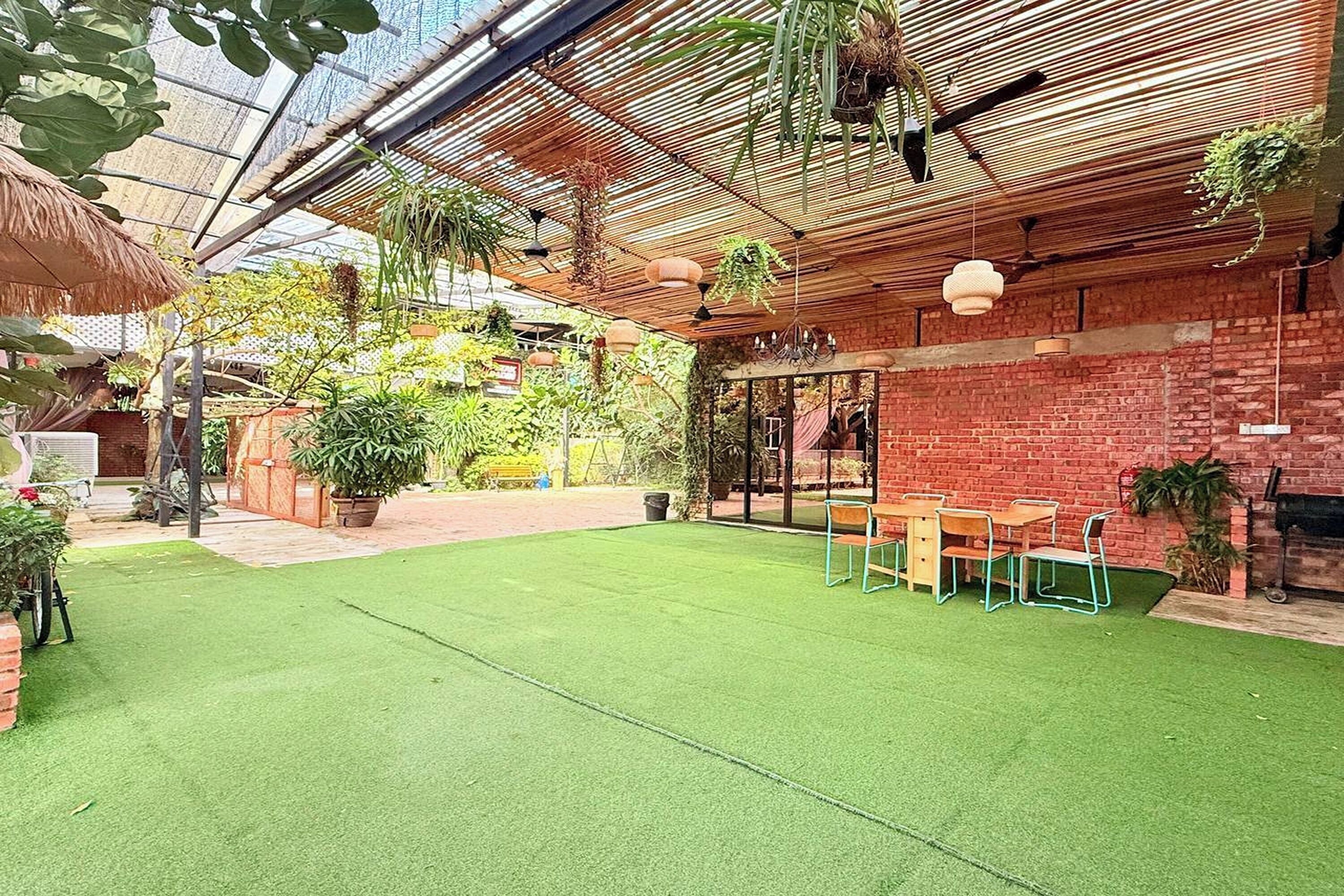 A covered patio with artificial grass, a brick wall, hanging plants, and a wooden table with chairs.