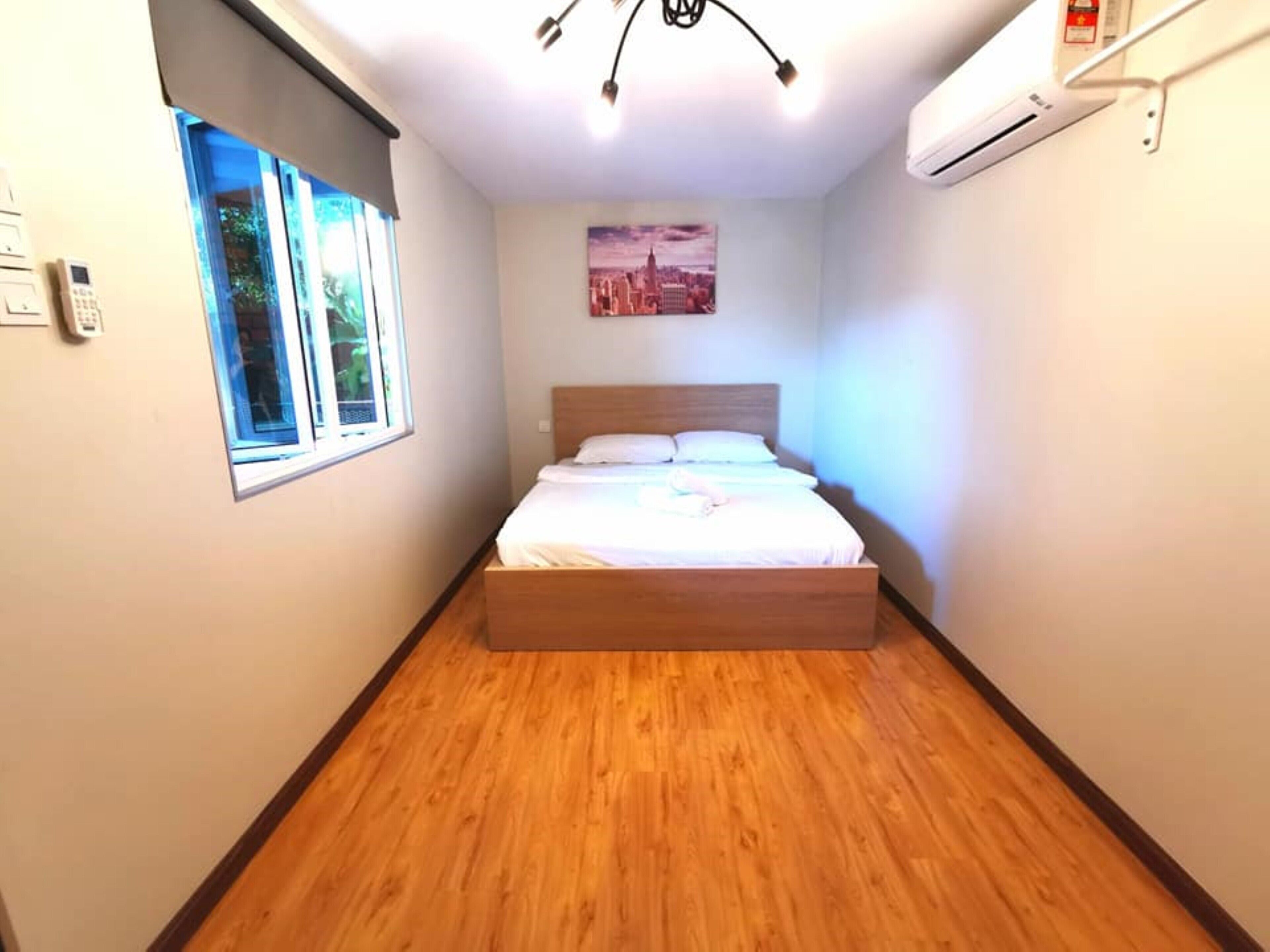 A bedroom with a wooden bed, a window, an air conditioner, and a cityscape painting on the wall.