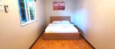 Un dormitorio con una cama de madera, una ventana, aire acondicionado y un cuadro de un paisaje urbano en la pared.