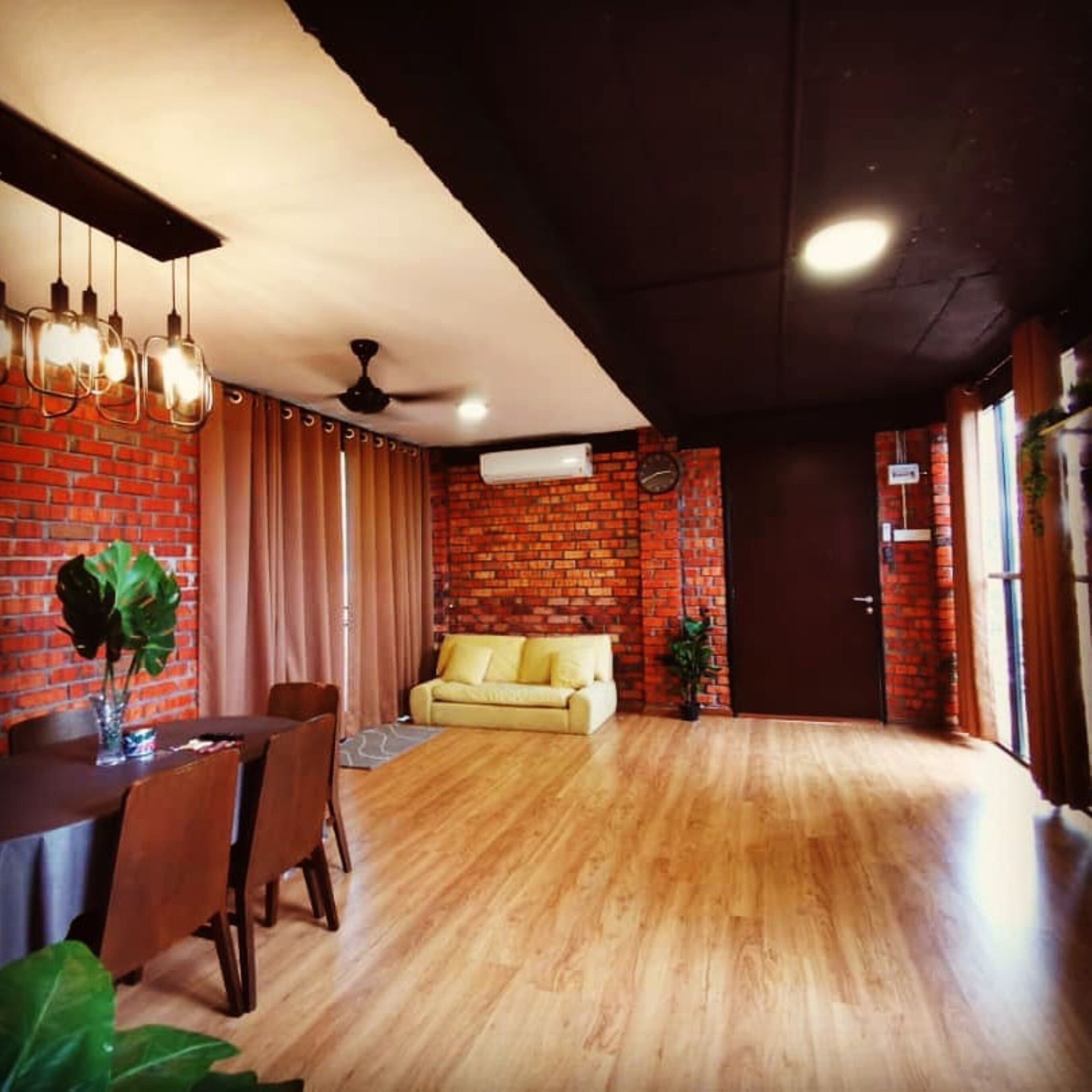 A modern living room with a wooden floor, a brick wall, a yellow sofa, and a dining area with a table and chairs.