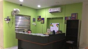 A reception desk with a green wall, a window with blinds, an air conditioning unit, and a security camera. - Ideal Hotel Sri Permaisuri Cheras (Kuala Lumpur)