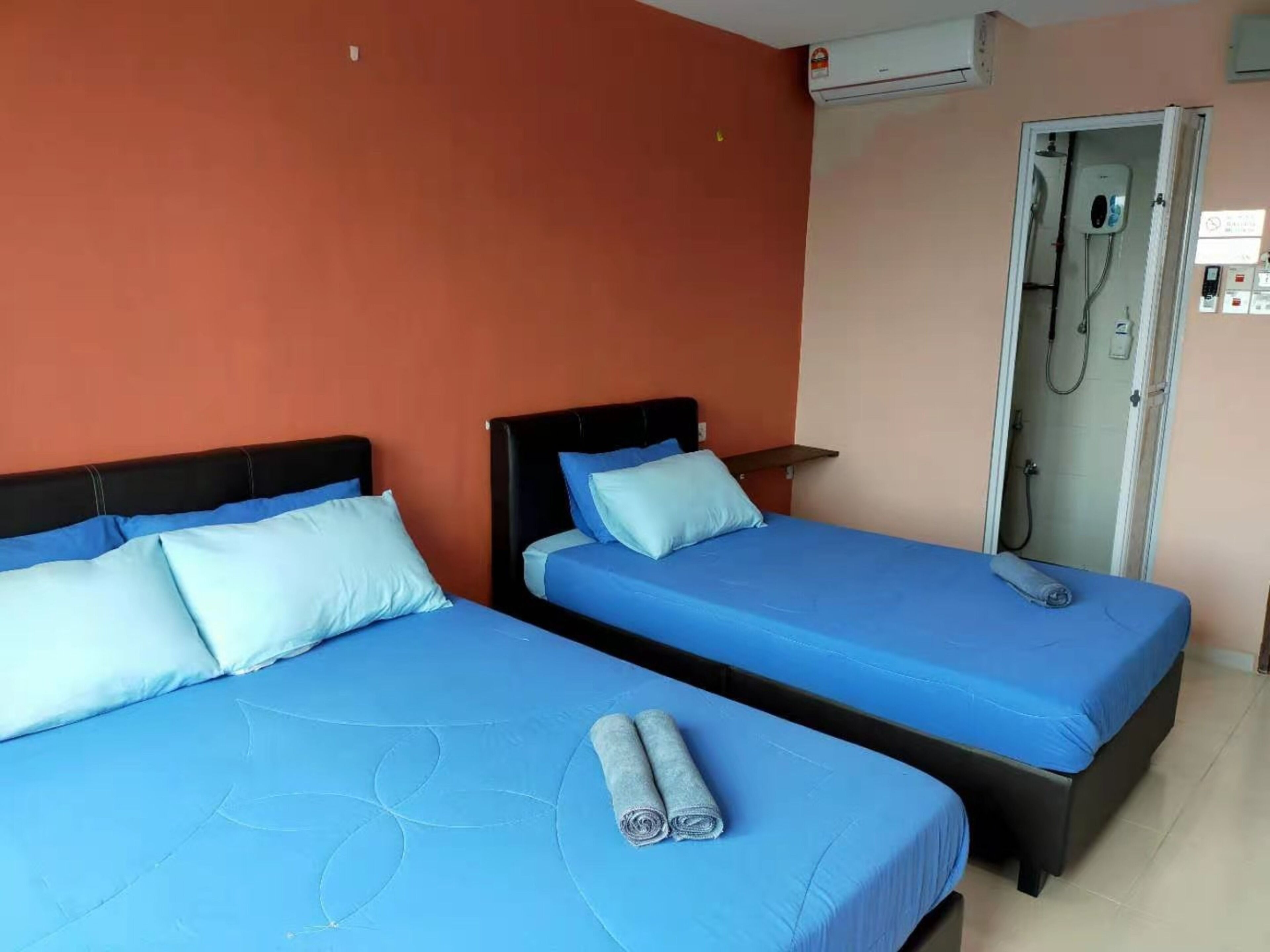 Two single beds with blue bedding, a small table, and a shower area.