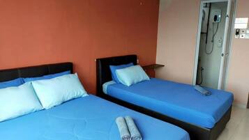 Two single beds with blue bedding, a small table, and a shower area.