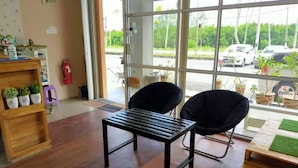 A room with a wooden floor, a black table, and two black chairs. There is a window with a view of parked cars and greenery outside. - CSH Motel Kuala Perlis (Kuala Perlis)