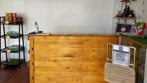 A wooden reception desk with a QR code for check-in, a shelf with canned goods, and a decorative rooster on a wall shelf. - CSH Motel Kuala Perlis (Kuala Perlis)