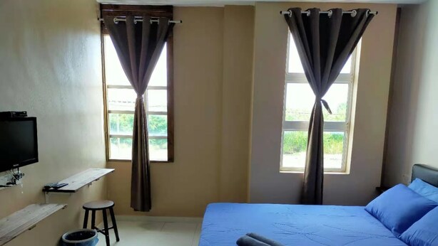 A bedroom with a bed, a TV, a small stool, and a window with curtains. - CSH Motel Kuala Perlis (Kuala Perlis)