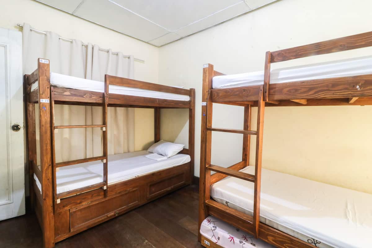 Quarto com duas camas beliche, piso de madeira e porta branca.