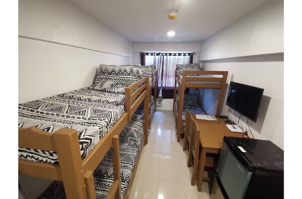 Una habitación pequeña con dos literas, un escritorio con computadora, televisión y ventana con cortinas.