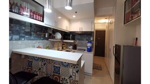 A modern kitchen with a white countertop, patterned backsplash, and hanging pendant lights. - SweetSuites at Pine Crest New Manila (Quezon City)