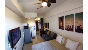 A modern hotel room with a bed, a sofa, a TV, a ceiling fan, and a cityscape artwork on the wall. - SweetSuites at Pine Crest New Manila (Quezon City)