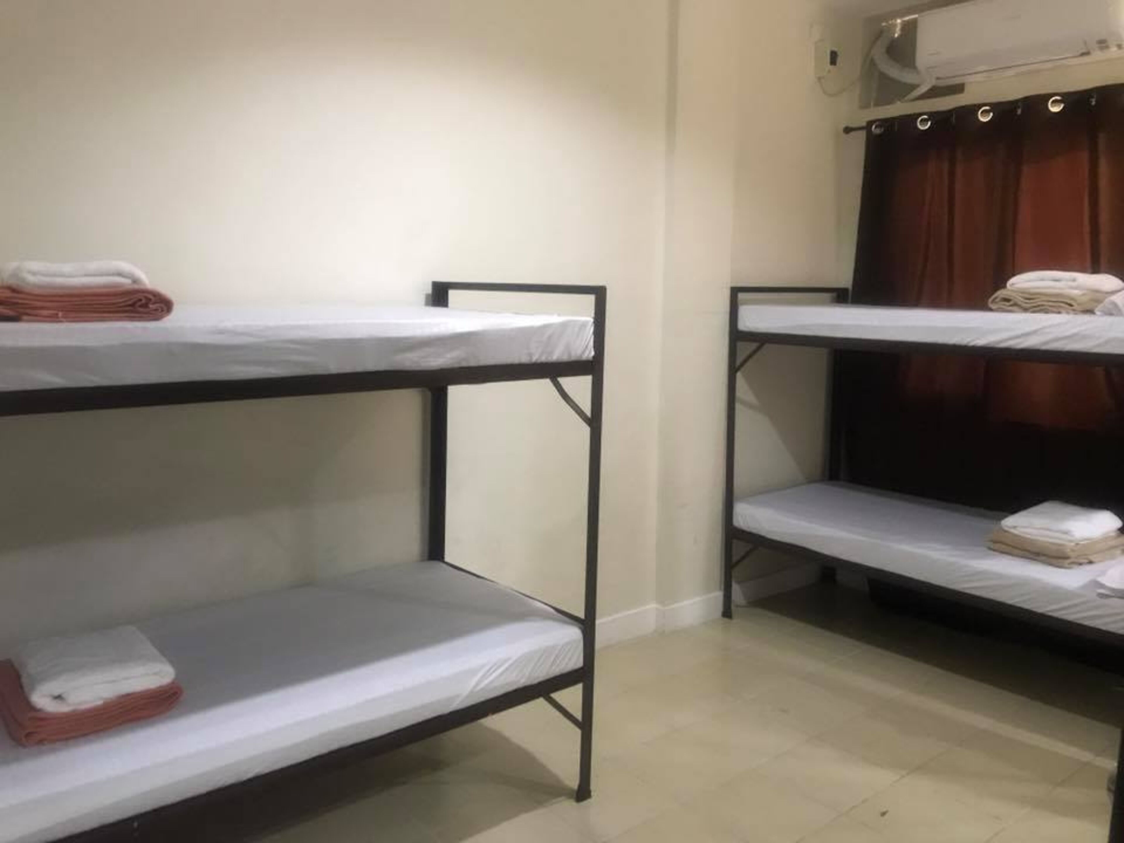 A dormitory room with bunk beds, a curtain, and an air conditioning unit.