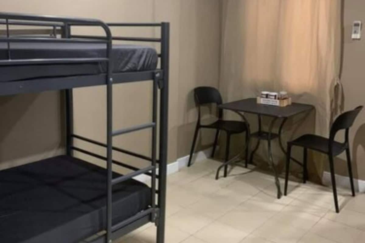 A bunk bed, a small table with chairs, and an air conditioning unit in a room with beige walls and tiled flooring.