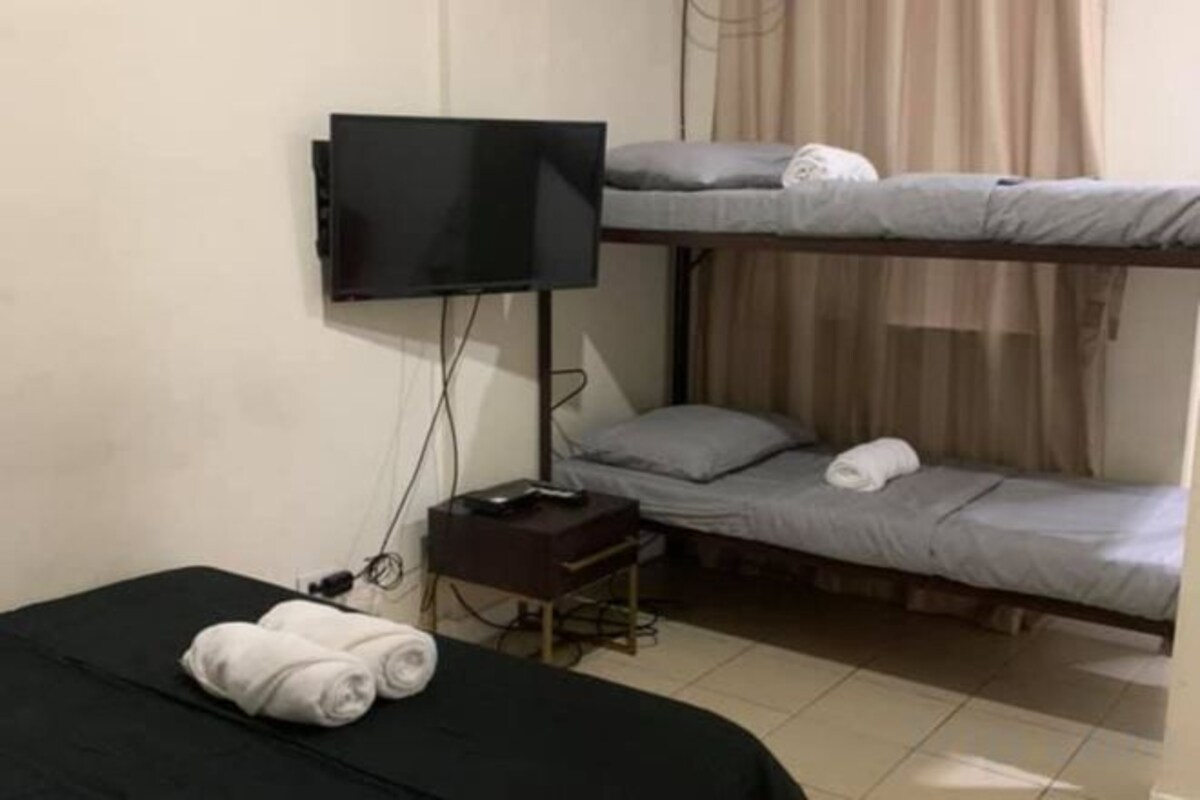Une chambre avec un lit simple, un téléviseur fixé au mur et un lit superposé au-dessus.