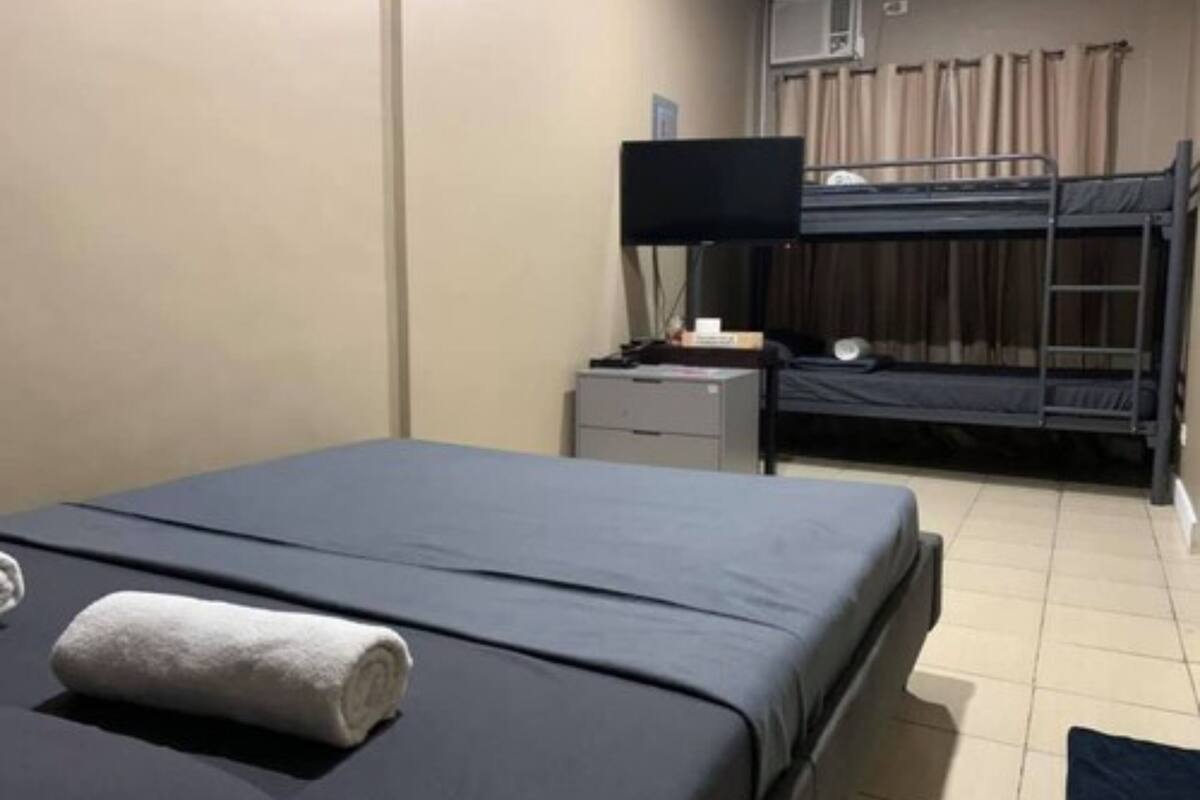 A hotel room with a bunk bed, a desk with a computer, a flat-screen TV, and a bed with a rolled towel.