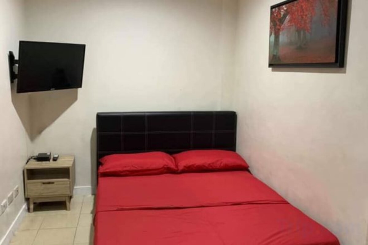 Une chambre à coucher avec un lit, une table de chevet, un téléviseur fixé au mur et un tableau.