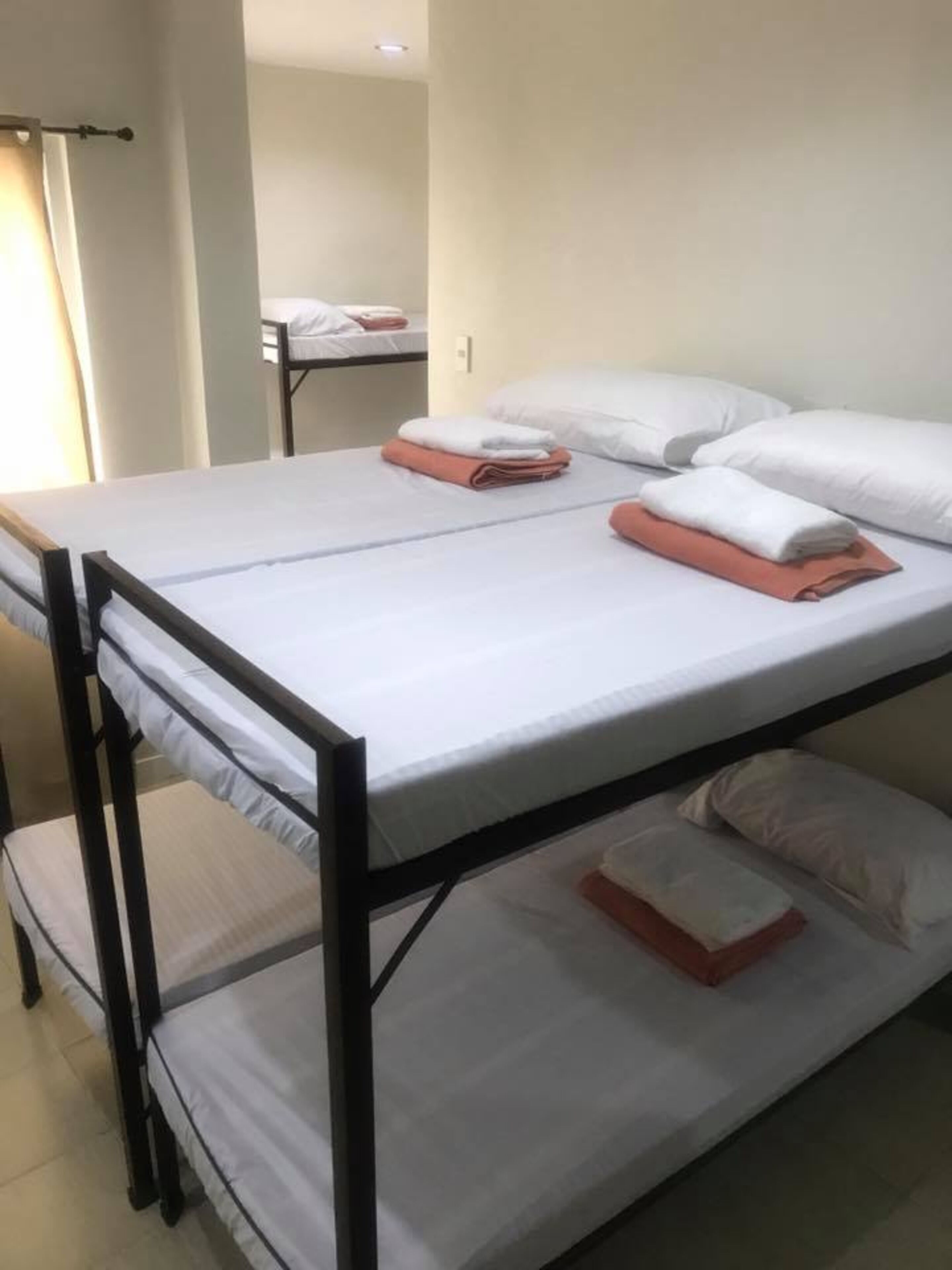 Un lit simple avec un cadre en métal, du linge de lit blanc et des serviettes orange.
