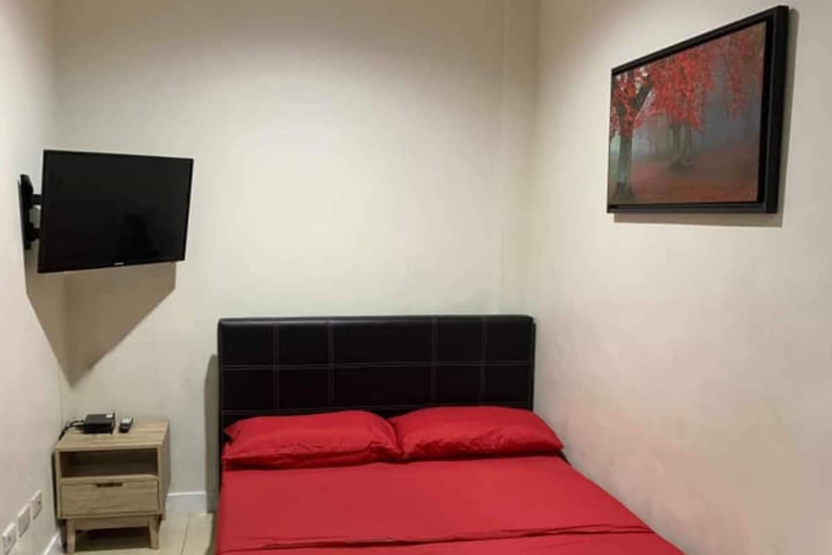 A bedroom with a bed, a nightstand, a TV mounted on the wall, and a framed picture.