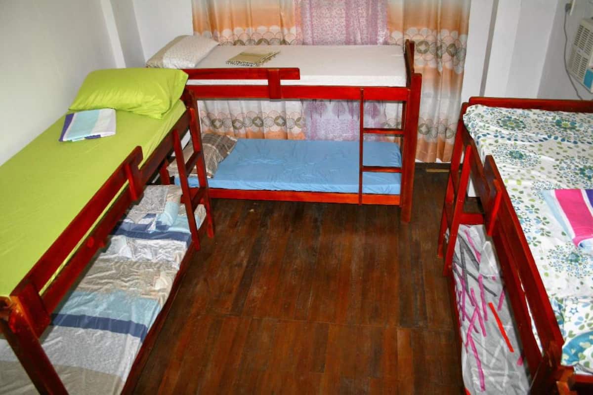 Ein kleiner, kompakter Raum mit zwei Etagenbetten und einem Einzelbett, Holzboden und einem Vorhang mit Blumenmuster.