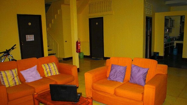 Eine Lobby mit zwei orangefarbenen Sofas, einem Holztisch mit einem Laptop und einem Feuerlöscher.