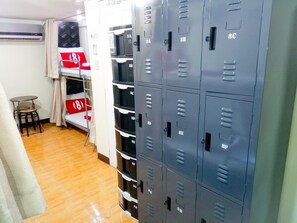 A room with multiple grey lockers, a small table with two chairs, and a bed with red and white bedding. - 8 Hostel at Quiapo (Manila)