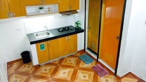 A compact kitchen with wooden cabinets, a sink, a stove, and a door marked "NESTROOM". - 8 Hostel at Quiapo (Manila)