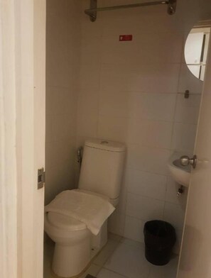 A small, basic bathroom with a toilet, a sink, and a black trash bin. - Rd Suites Greenbelt (Makati)
