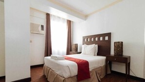 A hotel room with a bed, a bedside table, and a window with curtains. - Rd Suites Greenbelt (Makati)