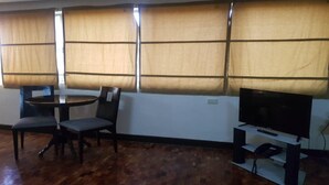 A room with a wooden floor, a round table with two chairs, a television on a stand, and large windows with curtains. - Rd Suites Greenbelt (Makati)